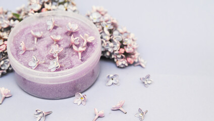 Face scrub on violet background with lilac flowers.