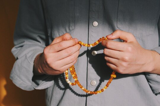hands of muslim man performing islamic ritual chanting / invocation / dhikr (with both hands) with orange rosary & background