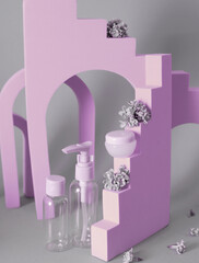 Group of cosmetic bottles with lilac on background with geometric beige shapes. Face scrub, gel shower and cream on violet background with lilac flowers.