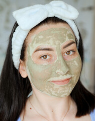 Beautiful young woman smears her face with cosmetic clay. Woman doing beauty treatments at home. Home face care concept. 