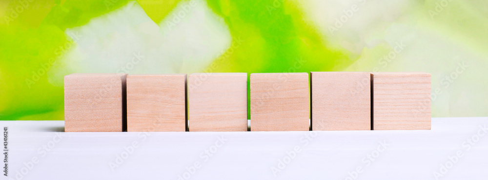 Poster a row of six empty wooden cubes on a blurred green-yellow background with copyspace for your text, l