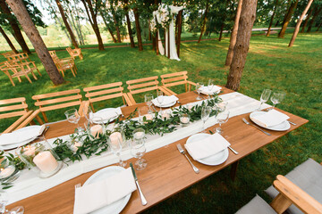 Table, chairs and wedding decoration in the forest. Green rustic decor with candles.