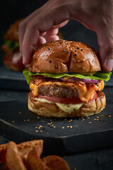 Vertical shot of a male's hand grabbing burger's upper bun