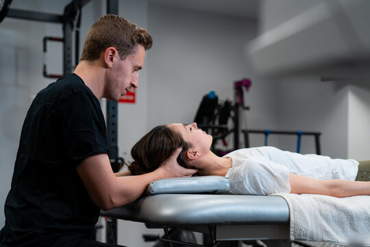 Side view of unshaven male physical therapist massaging neck of woman with closed eyes in hospital - Powered by Adobe