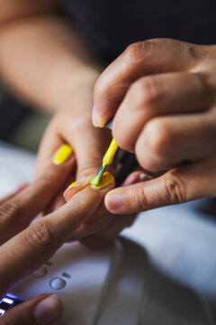 Crop female master applying yellow polish on nails of anonymous client in beauty salon