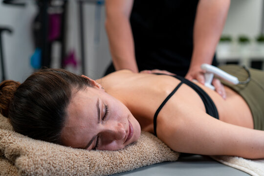 Male physiotherapist applying laser to back skin of female during medical treatment in hospital