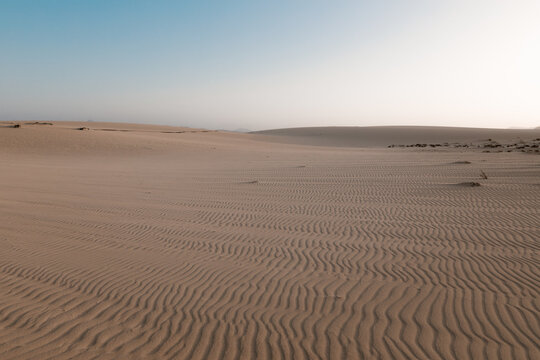 Picturesque view of dunes with uneven surface and sandy hills under light sky in desert