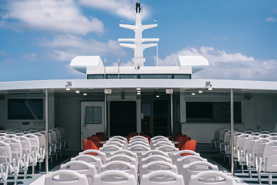 Deck of cruise boat with empty white chairs in row under clear sky with clouds