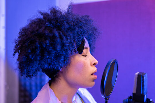 Black female singer performing song against microphone with pop filter while standing and closed eyes in sound studio