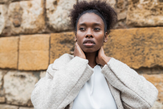 Portrait Of Attractive African American Female With Coat Standing In Historic City District On Warm Spring Day And Looking Away