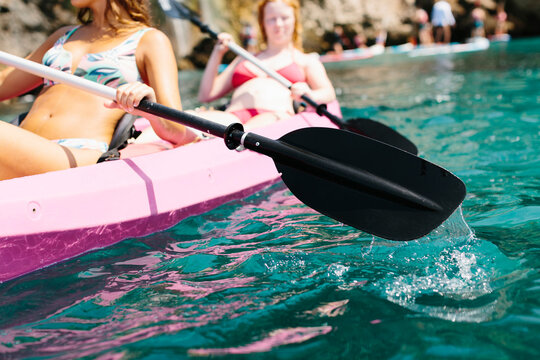 Side view travelers with paddles floating on turquoise seawater near the rocky shore on sunny day in Malaga Spain