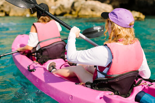 Back view travelers with paddles floating on turquoise seawater near the rocky shore on sunny day in Malaga Spain