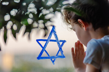 Little Jewish boy draws the Star of David sign on the window. The symbol of Israel. Solidarity ...