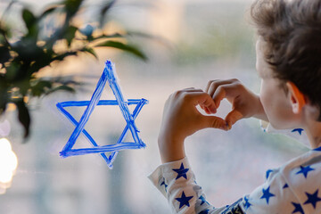 Little Jewish boy draws the Star of David sign on the window. The symbol of Israel. Solidarity...