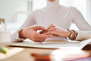 Crop unrecognizable female astrologist in rings and bracelets working at desk with paper album at home