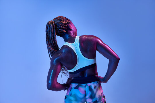 Back view of anonymous muscular African American female athlete with sweaty body showing biceps on blue background