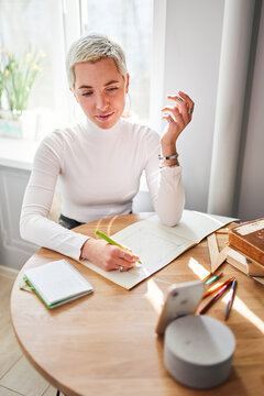 From above female astrologist taking notes in notepad at desk with cup of coffee at home in sunlight