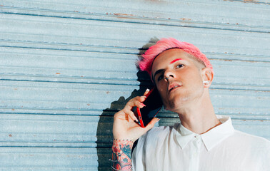 Transsexual man in trendy wear with tattoo and pink hair speaking on cellphone while looking away
