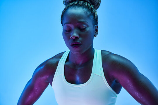 Young African American sportswoman with Afro braids in bun and closed eyes on blue background