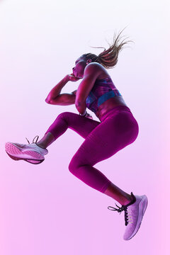 African American female athlete with flying hair in sports clothes jumping with clasped hands during training