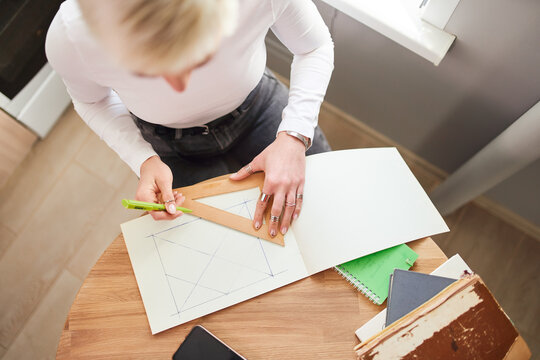 From above of crop unrecognizable female astrologist drawing on paper with triangle and pen at table