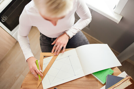 From above of crop unrecognizable female astrologist drawing on paper with triangle and pen at table