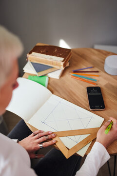 From above of crop unrecognizable female astrologist drawing on paper with triangle and pen at table