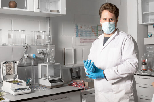 Male chemist in sterile mask and gloves looking at camera against moisture analyzer and analytical balance in cannabis laboratory