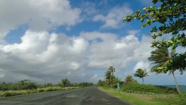 POV Driving along two lane road on tropical island against blue sky and clouds