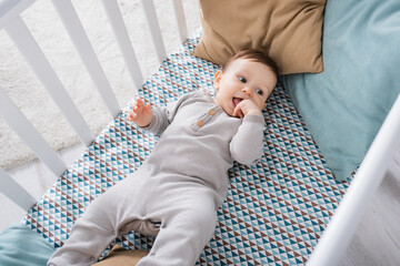high angle view of infant boy in romper lying in baby crib