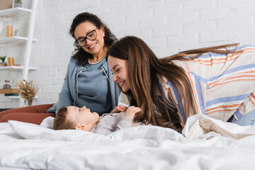 happy mother tickling baby boy near african american woman in glasses