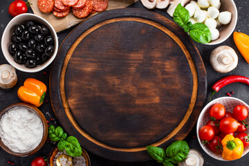 Pizza ingredients on the dark background and round cutting board, free space for text. Pepperoni,...