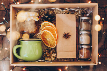 Gift box with tea set. Tea, cup, jam or honey, spices, dried oranges, anise in box on wooden table...