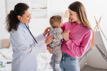 Fototapeta premium african american pediatrician examining infant boy in hands of happy mother