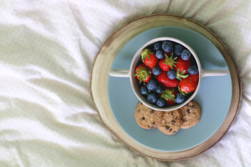 Bowl of blueberries and strawberries and chocolate chip cookies on a bed. Flat lay.