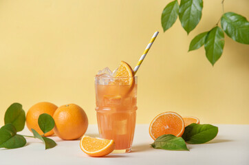 A glass of refreshing orange juice with a slice of orange and ice on a yellow background with juicy...