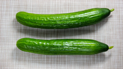 Two whole fresh cucumbers on a light background.