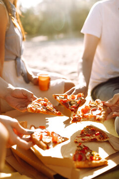 Hands taking slices of pizza close view. Friends eating pizza at the beach. Fast food concept. Beach holiday and summer vacation concept.