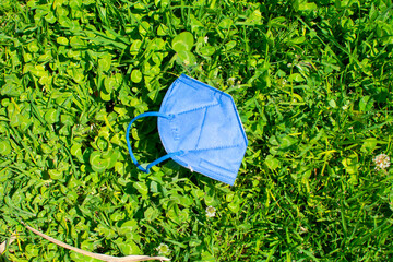 covid 19 blue FFP2 mask lying on the grass on a sunny day. - obrazy, fototapety, plakaty