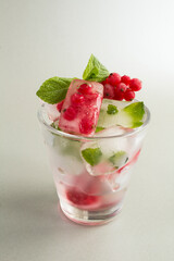 Ice with frozen berry and mint in the drinking glass on the gray background. Location vertical.