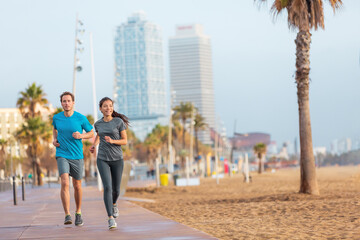 Fototapeta na wymiar Running man and woman couple jogging on Barcelona Beach, Barceloneta. Healthy lifestyle people runners training outside on boardwalk. Multiracial couple, Asian woman, Caucasian fitness man working out