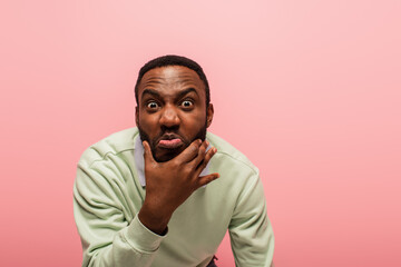 African american man grimacing at camera isolated on pink