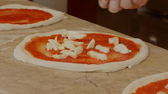 Chef preparing neapolitan margherita pizza with tomato sauce and mozzarella cheese, adding mozzarella cheese on raw dough.