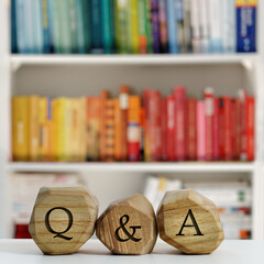 Letters Q and A written on wooden irregular blocks in front of blurred bookshelf.
