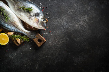 Fresh fish dorado on black stone table with ingredients for cooking. Top view with copy space.