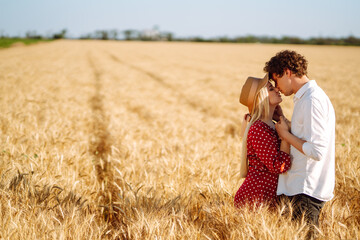 Naklejka na ściany i meble Loving couple in the in a wheat field. Enjoying time together. The concept of youth, love and lifestyle.