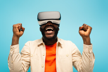 Fototapeta premium african american man screaming and showing success gesture while gaming in vr headset isolated on blue