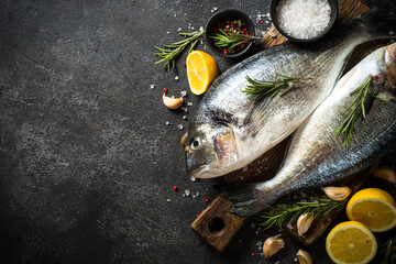 Dorado, raw fish on black stone table with ingredients for cooking. Top view with copy space.