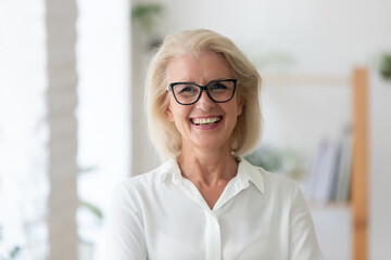 Headshot portrait of smiling senior Caucasian businesswoman in glasses pose in office on working...