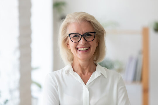 Headshot portrait of smiling senior Caucasian businesswoman in glasses pose in office on working day. Close up profile picture of happy middle-aged female employee or CEO show success at workplace.